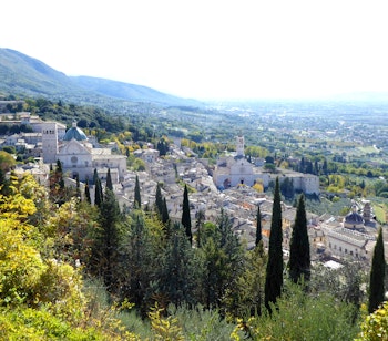 Panoramaudsigt over Assisi i Umbrien, Italien, hvor den historiske by med Basilica Santa Chiara ligger smukt på bjergsiden omgivet af cyprestræer og efterårsfarver