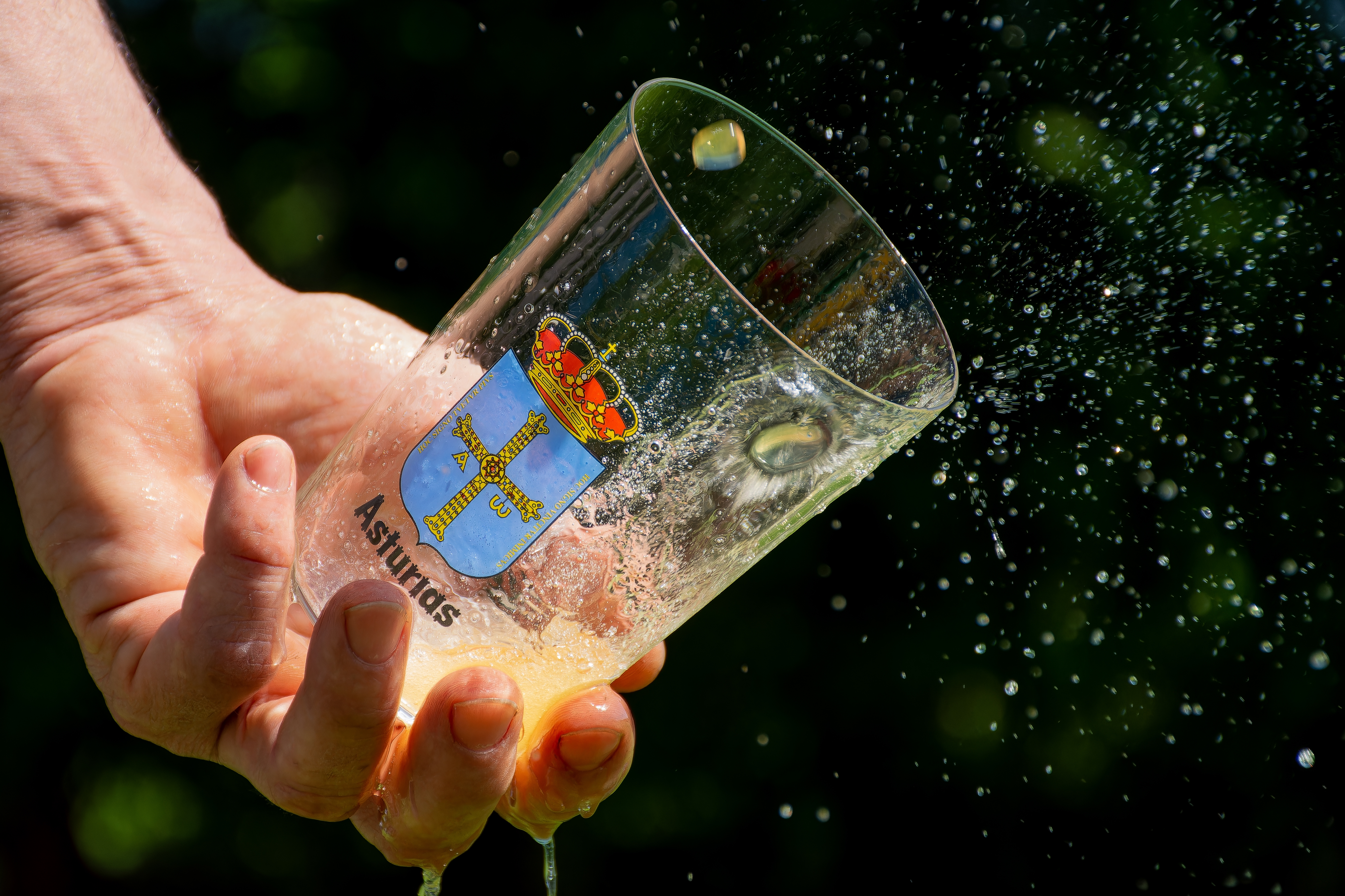 Hånd holder glas med frisk asturisk cider og vandstænk under Spaniens-ferie