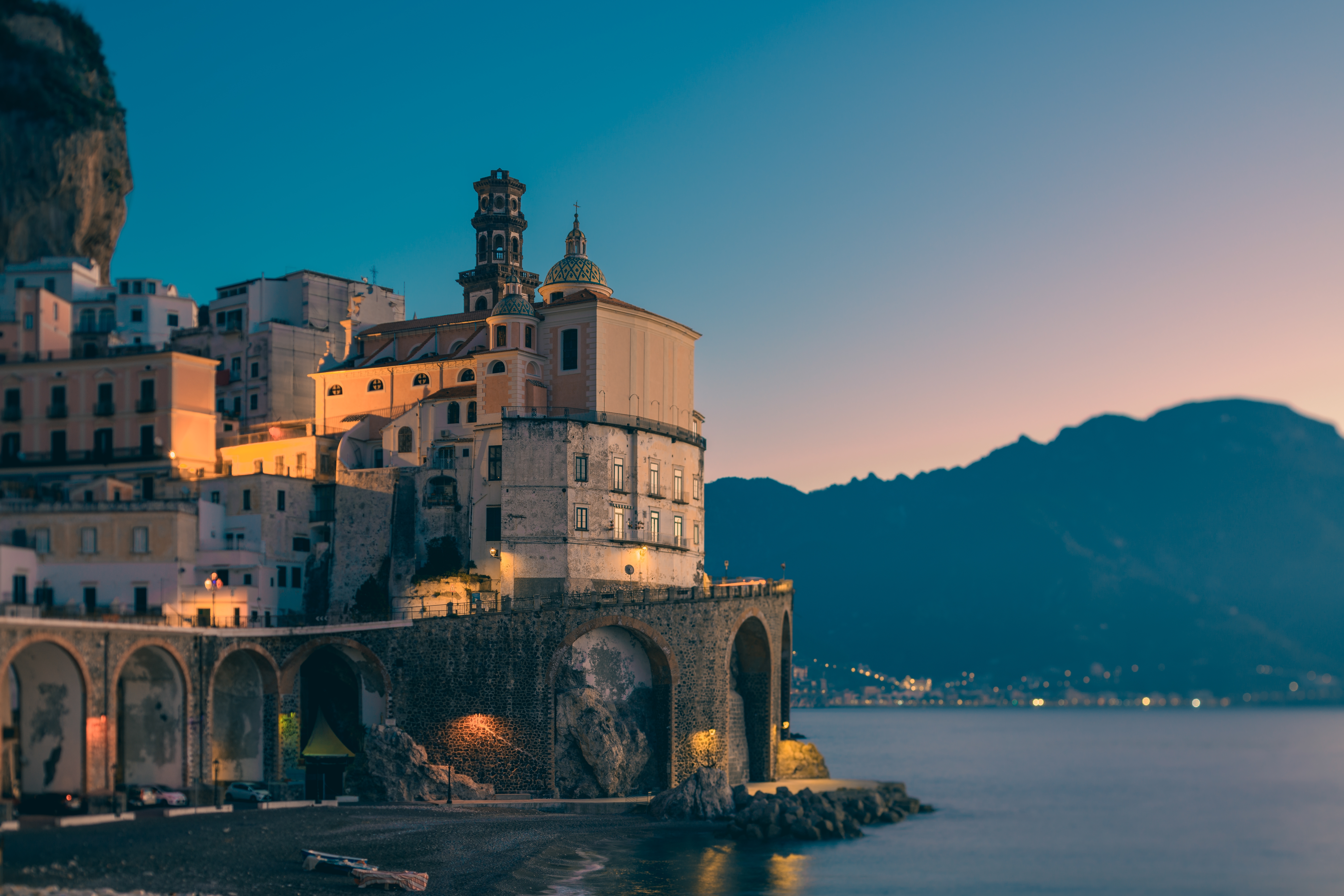 Aftenstemning over Atrani på Amalfikysten med den oplyste katedral, historiske stenbuer ud mod havet og bjerge i baggrunden