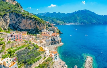 Luftfoto af den maleriske by Atrani ved Amalfikysten i Italien med farverige bygninger mellem bjergene og det azurblå Middelhav