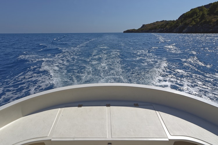 Kølvand fra båd på blåt hav langs sydkysten af Cilento Nationalpark i Italien med smuk kystlinje i horisonten under klar sommerhimmel