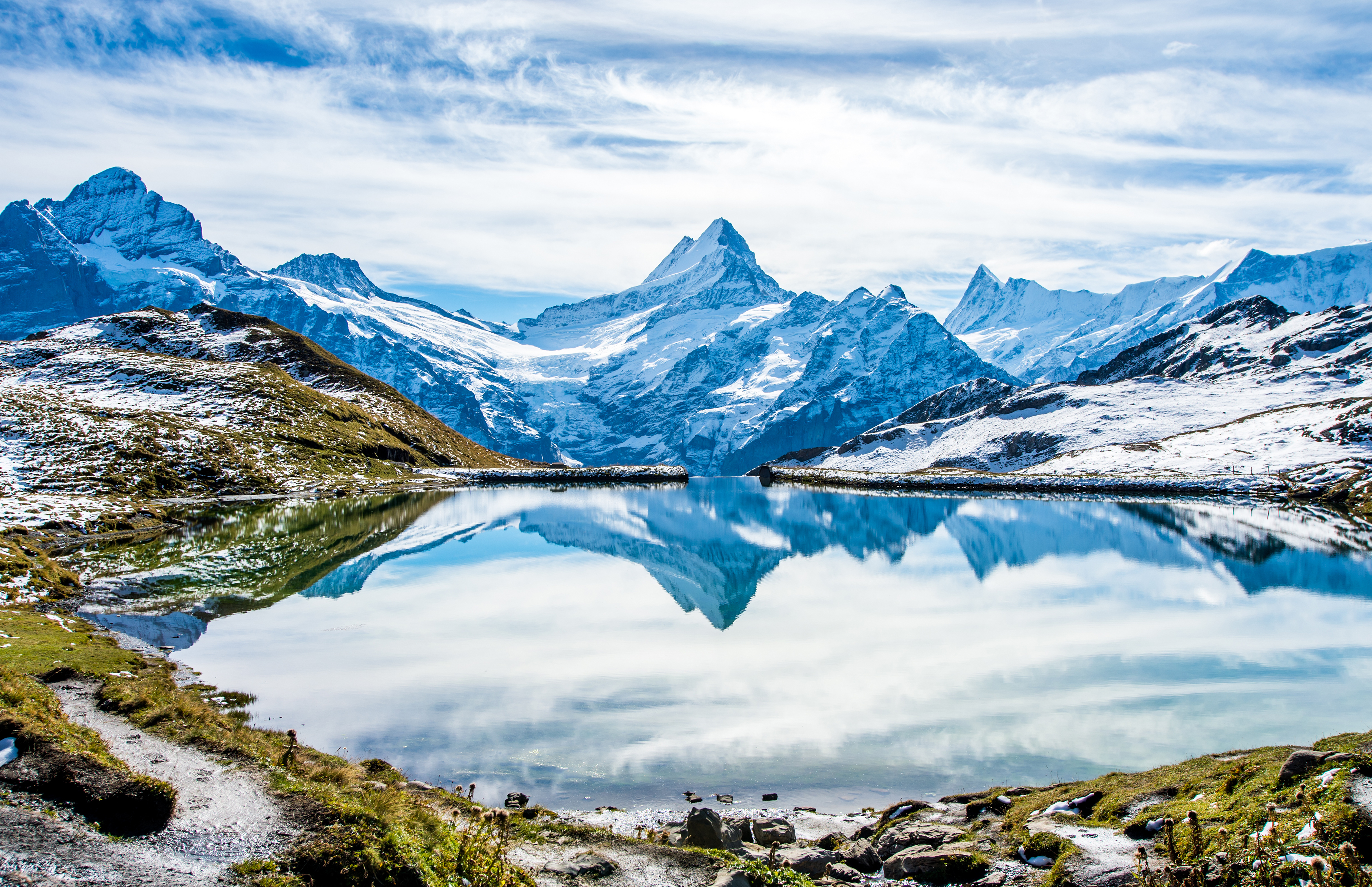 Betagende spejling af sneklædte schweiziske alper i Bachalpsees krystalklare vand, en idyllisk bjergso over Grindelwald med frodige grønne enge i Berner Oberland-regionen