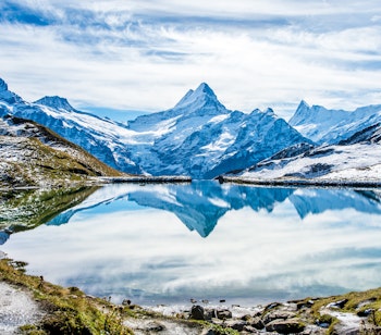 Betagende spejling af sneklædte schweiziske alper i Bachalpsees krystalklare vand, en idyllisk bjergso over Grindelwald med frodige grønne enge i Berner Oberland-regionen