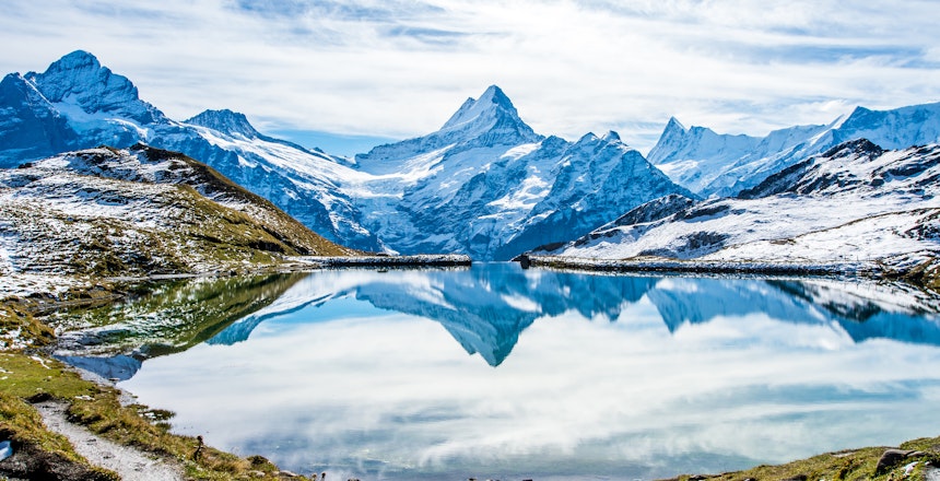 Betagende spejling af sneklædte schweiziske alper i Bachalpsees krystalklare vand, en idyllisk bjergso over Grindelwald med frodige grønne enge i Berner Oberland-regionen