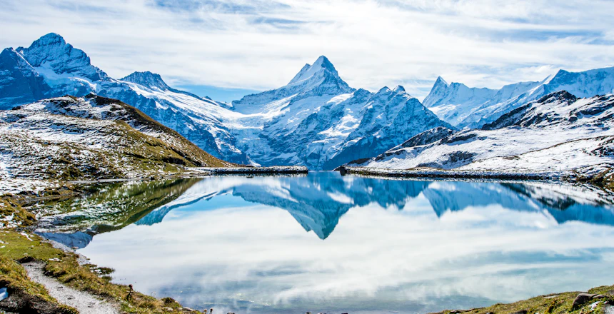 Betagende spejling af sneklædte schweiziske alper i Bachalpsees krystalklare vand, en idyllisk bjergso over Grindelwald med frodige grønne enge i Berner Oberland-regionen