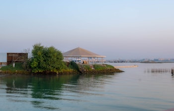 Idyllisk morgenvy over Bahrains kyst med traditionelle fiskerbåde og bygninger badet i det gyldne solopgangslys