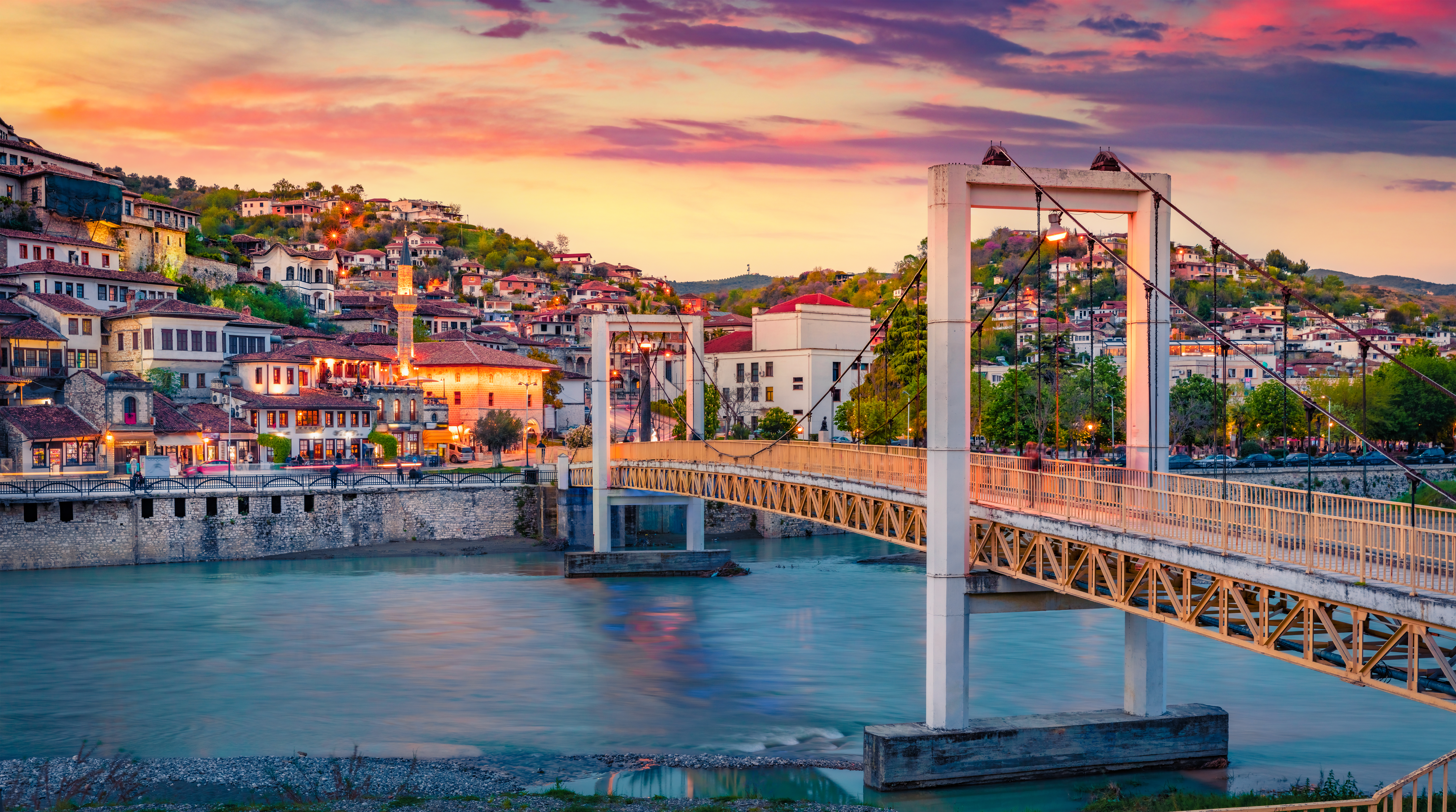 Smuk solnedgang over farverige huse og bro i pittoresk balkan by ved turkisblå flod