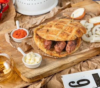 Traditionel balkanret med čevapi - saftige grillede pølser af hakket kød serveret med fladbrød, hakkede løg, rød ajvar-sauce og cremet kajmak på et rustikt træbræt