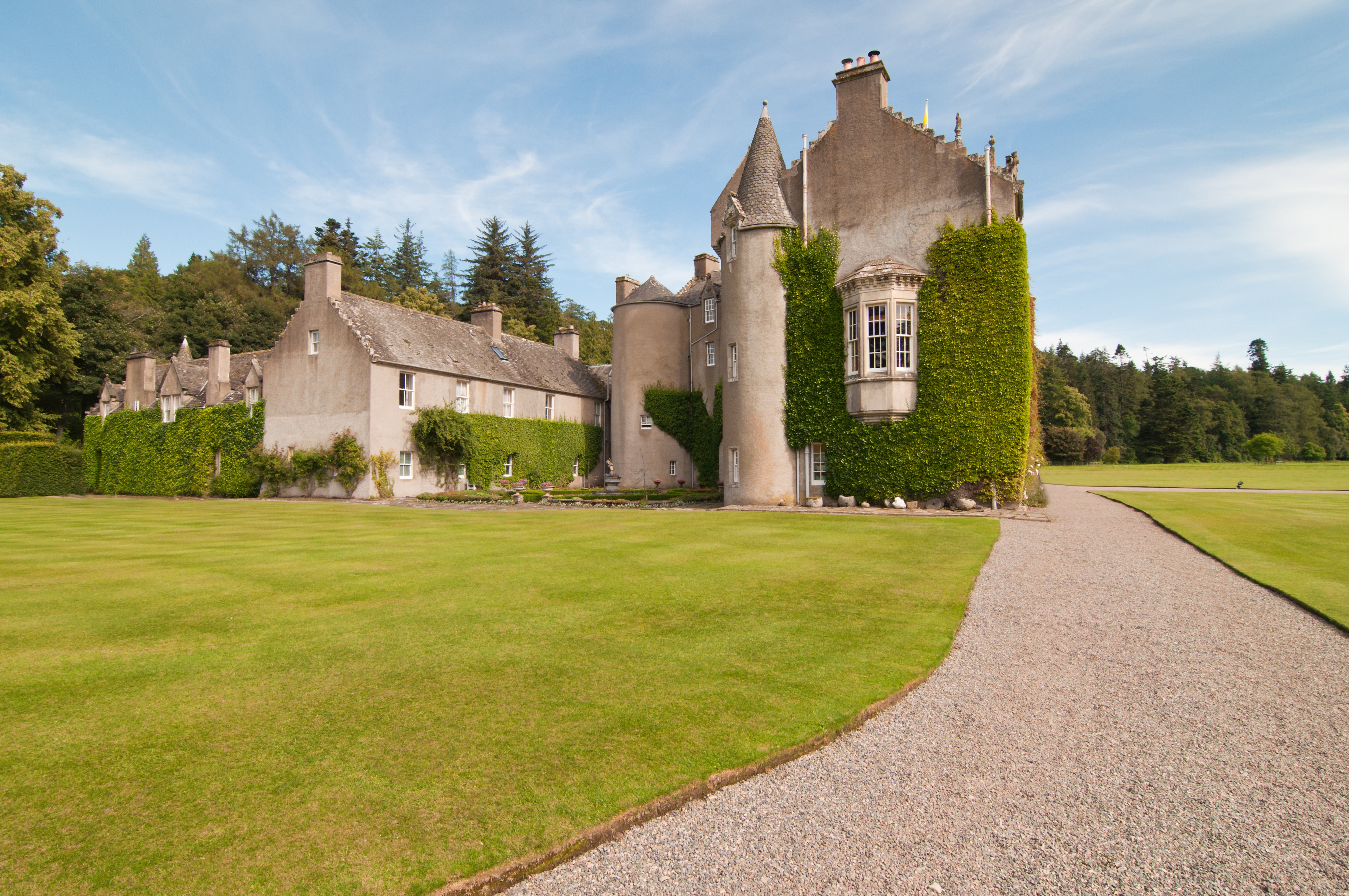 Ballindalloch Castle i Skotland med grønne plæner og vedbend-dækkede tårne langs en grusvej til det historiske skotske slot