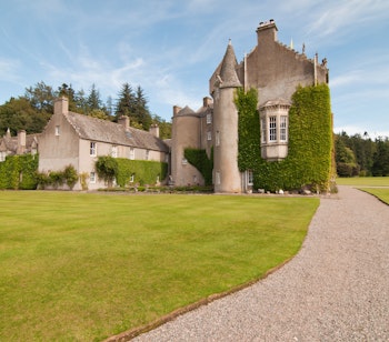 Ballindalloch Castle i Skotland med grønne plæner og vedbend-dækkede tårne langs en grusvej til det historiske skotske slot
