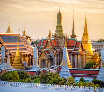 Betagende udsigt over Grand Palace og Wat Phra Kaew templet i Bangkok ved solnedgang, med gylden belysning på de ornamenterede bygninger og forgyldte spir