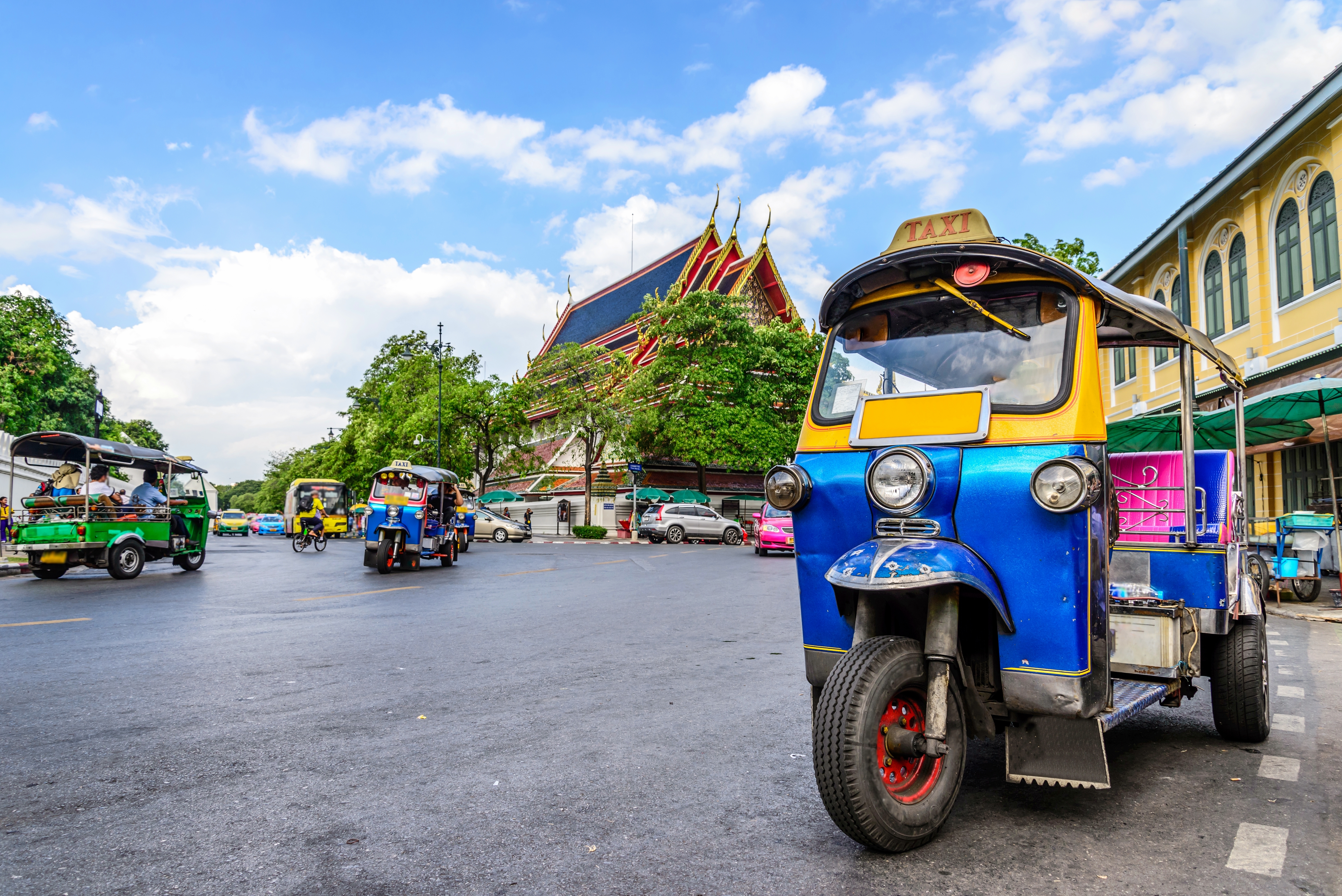 Farverig tuk-tuk taxi på gade i Bangkok med thailandsk tempel i baggrunden