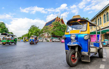 Farverig tuk-tuk taxi på gade i Bangkok med thailandsk tempel i baggrunden