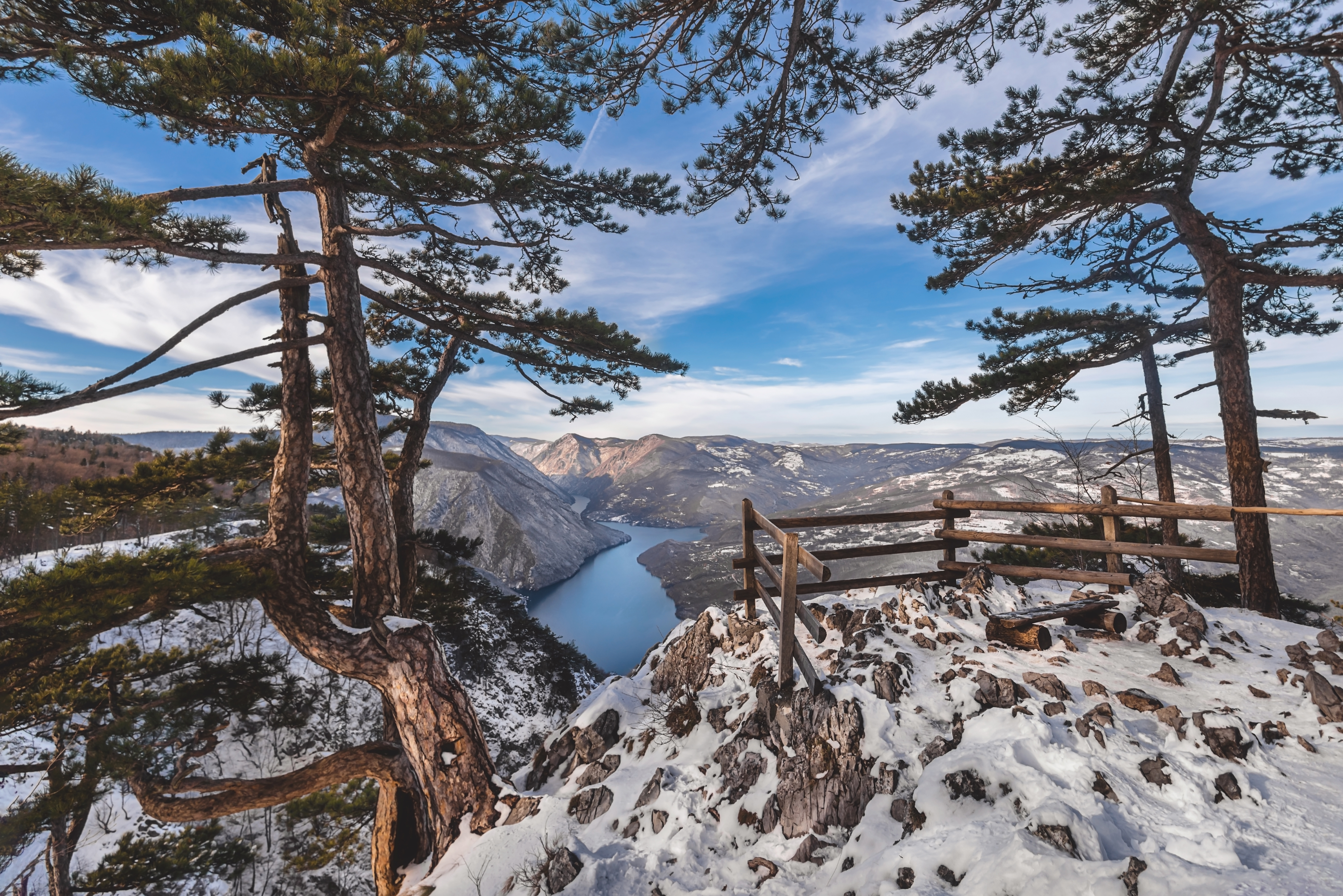 Banjska Stena udsigtspunkt i Serbien om vinteren med panoramaudsigt over Drina-floden og Perucac-søen dækket af sne, med træbænk og sikkerhedshegn