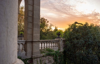 Betagende solnedgangsudsigt over den imponerende Cascada Monumental fontæne i Parc de la Ciutadella i Barcelona, med dens storslåede trappe, skulpturer og vandløb badet i gyldent aftenlys mod parkens frodige grønne omgivelser