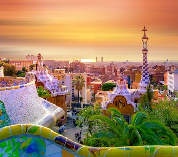 Betagende udsigt over Barcelona fra Park Güells farverige mosaikbænk ved solopgang med byens skyline i baggrunden