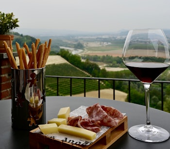 Italiensk aperitivo med et glas Barolo-vin, lokale oste og charcuteri med udsigt over de maleriske vinmarker i Piemonte-regionen