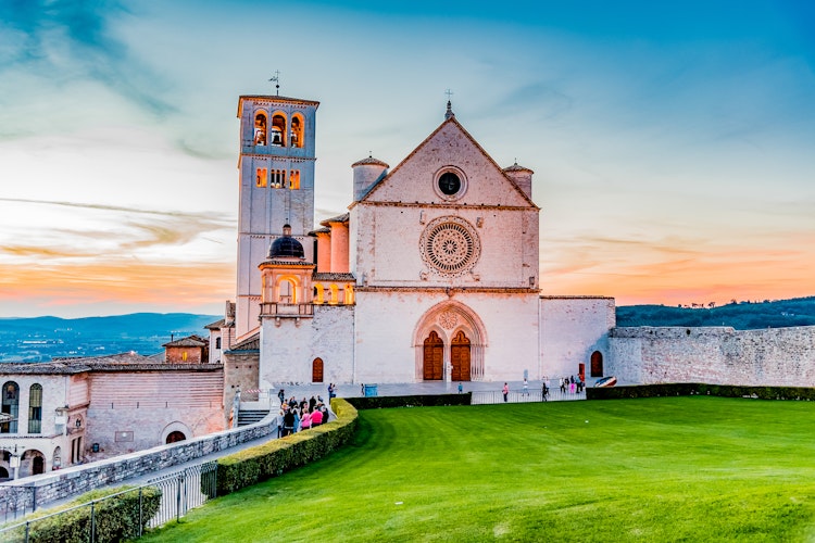 Den majestætiske San Francesco-basilika i Assisi badet i gyldent solnedgangslys - et UNESCO verdensarvssted med berømte fresker af Giotto og Cimabue, som vi besøger på vores sidste cykeldag