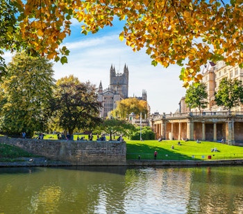 Bath Abbey og floden Avon i efterårsfarver med gyldne træer, der indrammer den historiske katedral og flodpromenaden i Bath, England