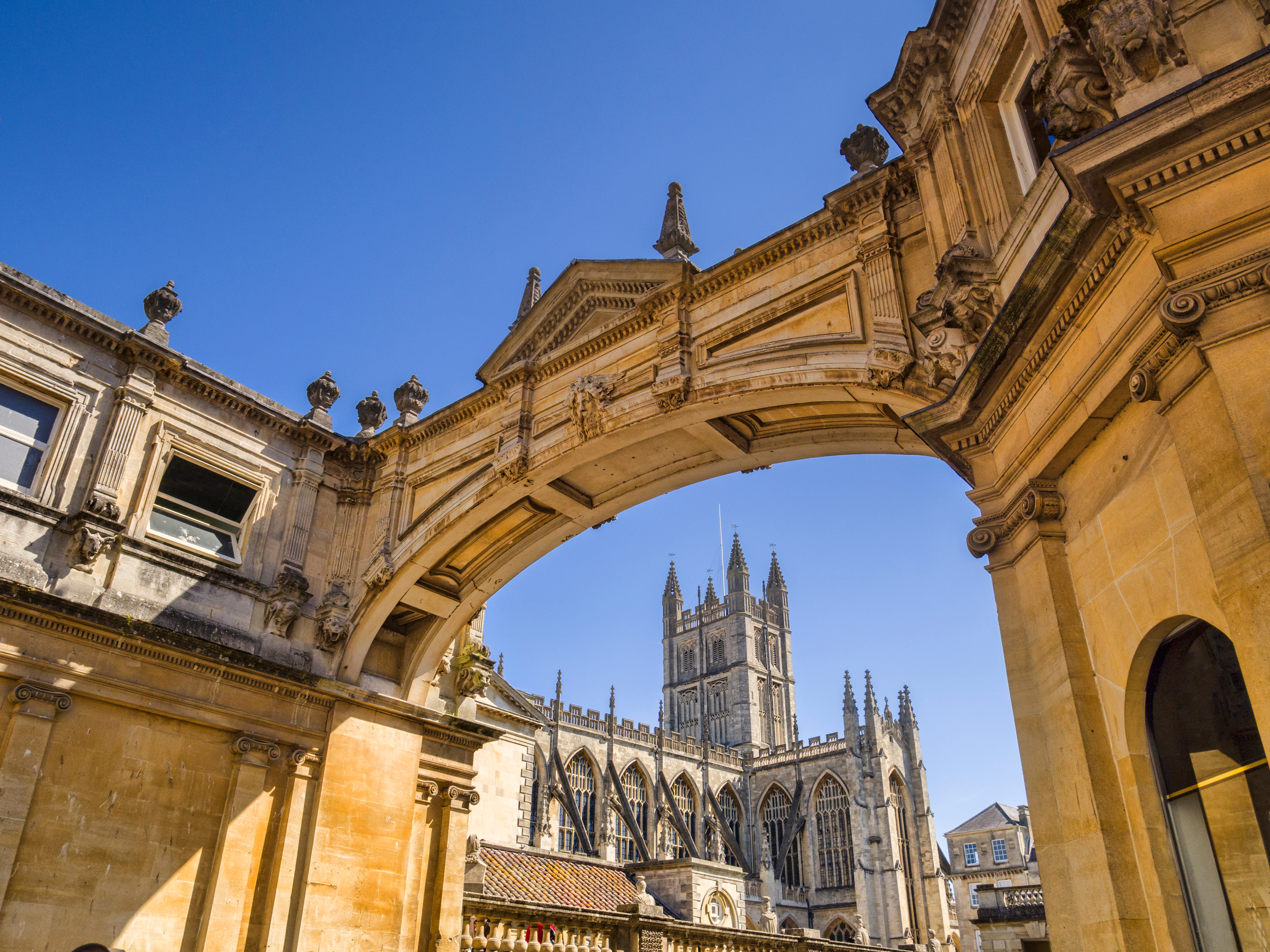 Bath Abbey set gennem smuk bue fra de romerske bade med gylden sten arkitektur under blaa himmel i England