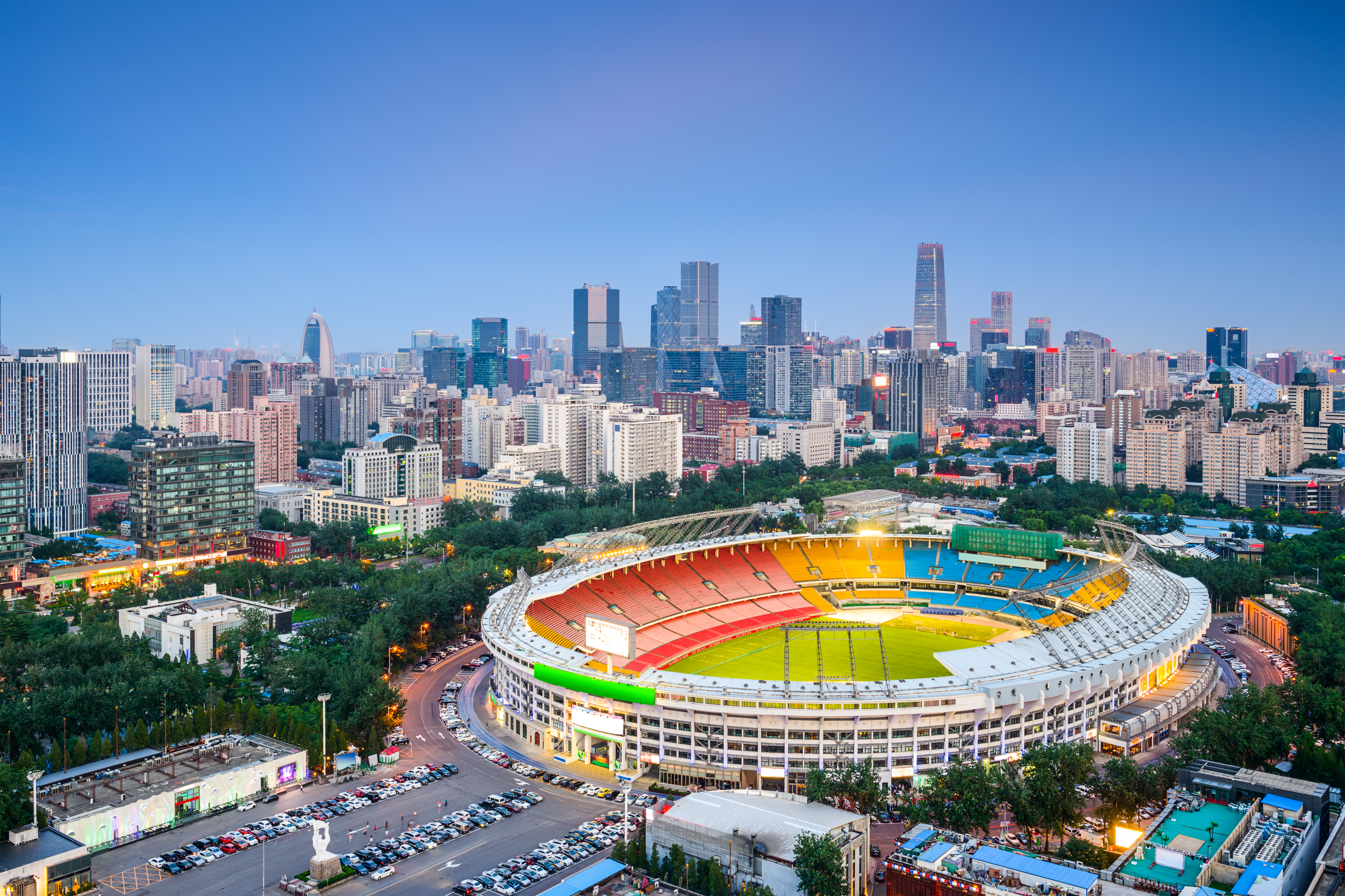 Beijing Workers Stadium oplyst ved skumring med moderne byskyline og skyskrabere i baggrunden