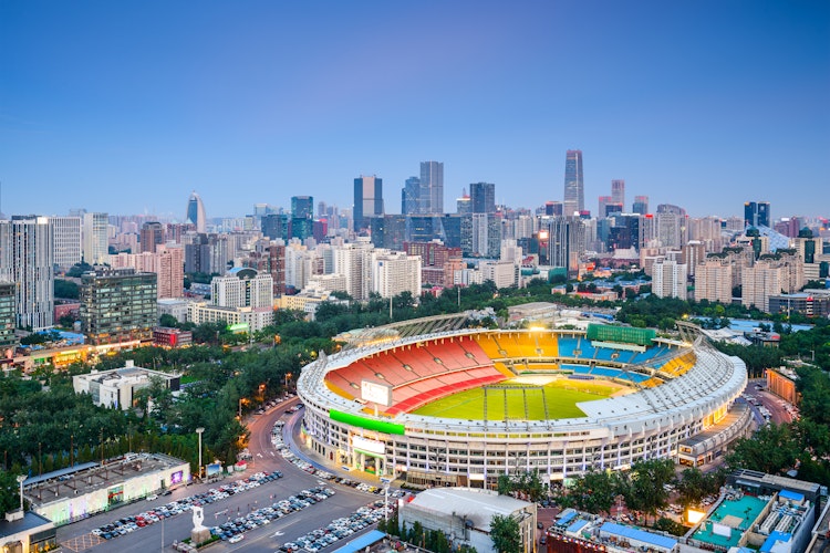 Beijing Workers Stadium oplyst ved skumring med moderne byskyline og skyskrabere i baggrunden