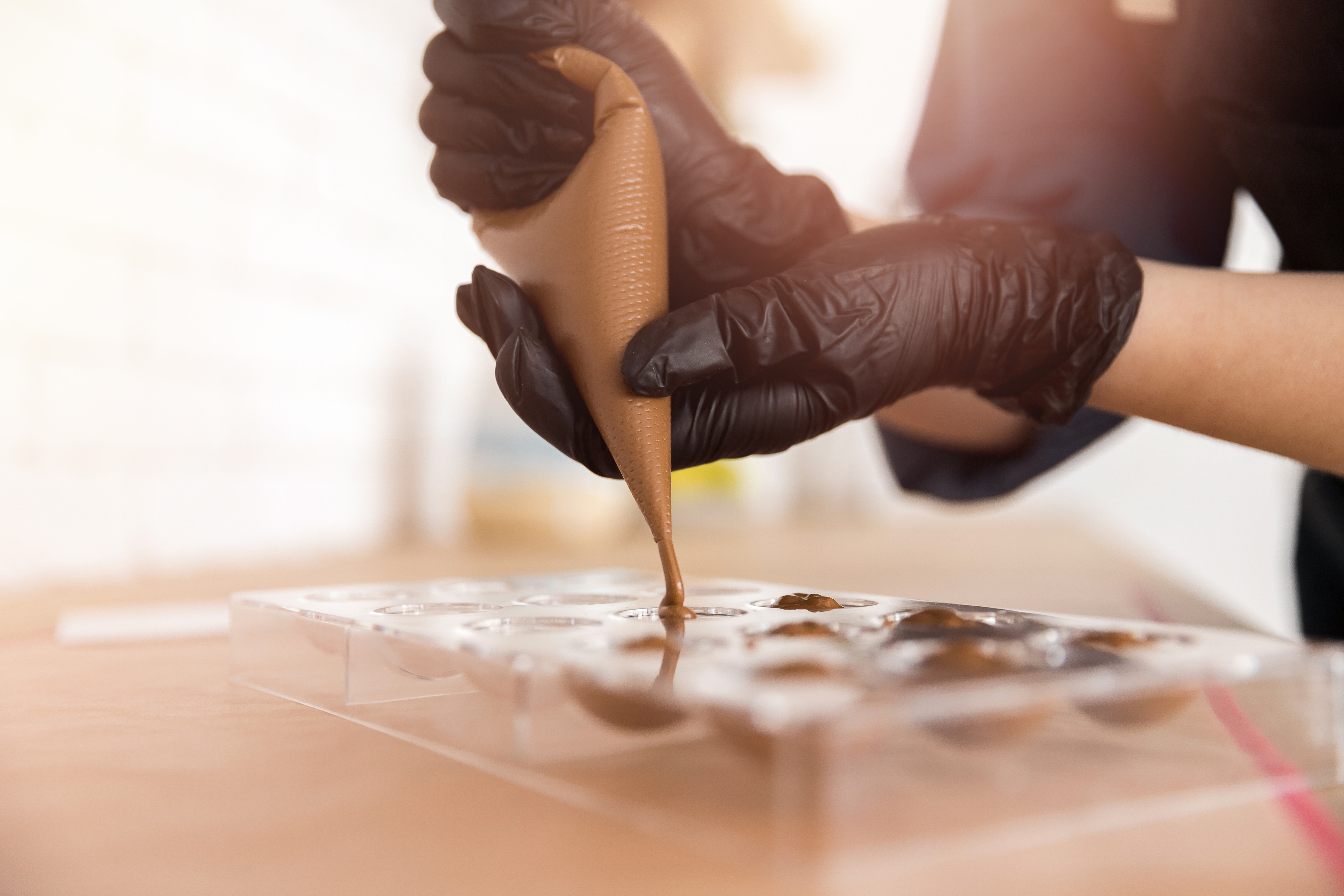 Professionel chokolatier fylder pralineforme med chokolade ved hjælp af en sprøjtepose under en chokoladeworkshop i Belgien