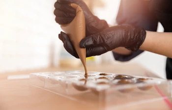Professionel chokolatier fylder pralineforme med chokolade ved hjælp af en sprøjtepose under en chokoladeworkshop i Belgien