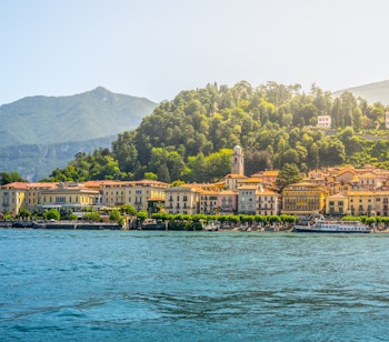 Malerisk udsigt over Bellagios farverige bygninger ved bredden af den azurblå Comosø, omgivet af grønne bjerge i Lombardiet på en solrig sommerdag