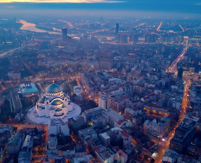 Luftfoto af Beograd i skumringen med den oplyste Saint Sava kirke, der dominerer byens skyline