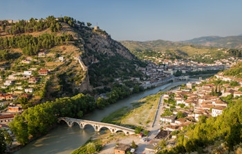 Betagende panoramaudsigt over Berats historiske by i Albanien med de karakteristiske hvide huse der kaskader ned ad bjergsiden, Osum-floden der slynger sig gennem dalen, og frodige grønne bjerge i baggrunden