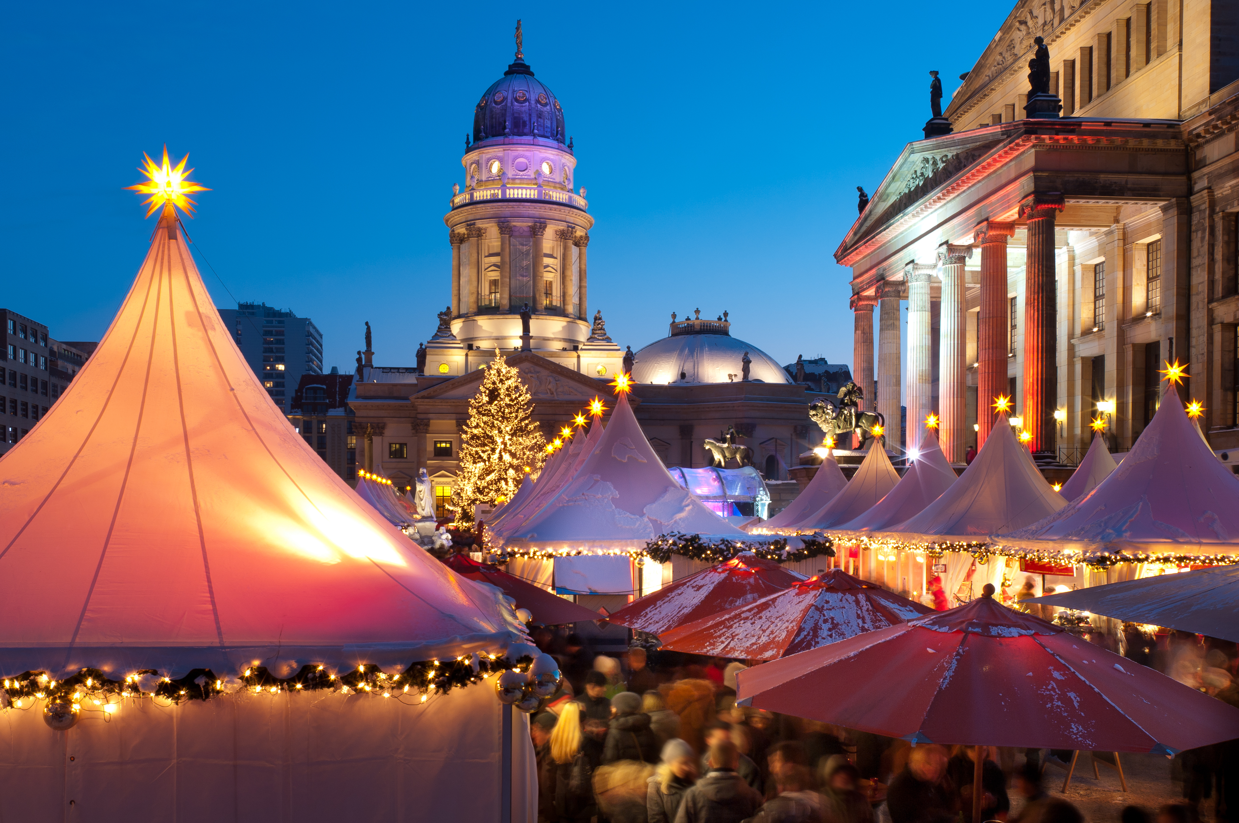 Stemningsfuldt julemarked på Gendarmenmarkt i Berlin med oplyste telte, juletræ og historiske bygninger i aftenlys