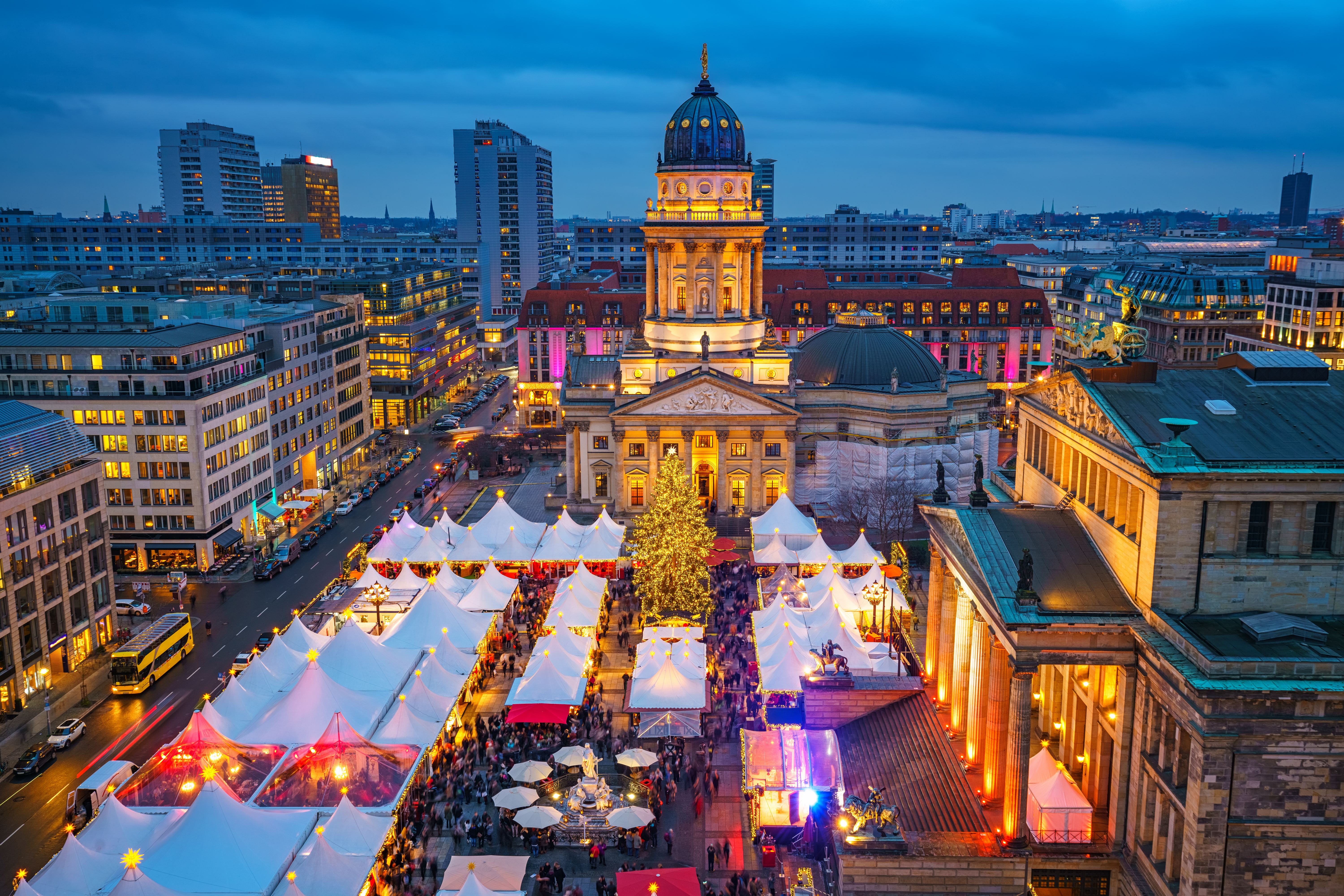 Stemningsfuldt julemarked på Gendarmenmarkt i Berlin med festlige hvide boder og et pyntet juletræ. I baggrunden ses den oplyste Deutscher Dom og Konzerthaus, der skaber en magisk julekulisse i den tyske hovedstad