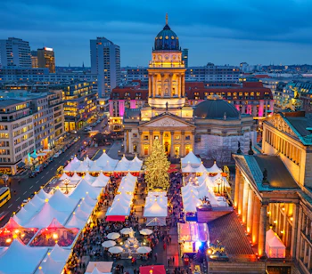 Stemningsfuldt julemarked på Gendarmenmarkt i Berlin med festlige hvide boder og et pyntet juletræ. I baggrunden ses den oplyste Deutscher Dom og Konzerthaus, der skaber en magisk julekulisse i den tyske hovedstad