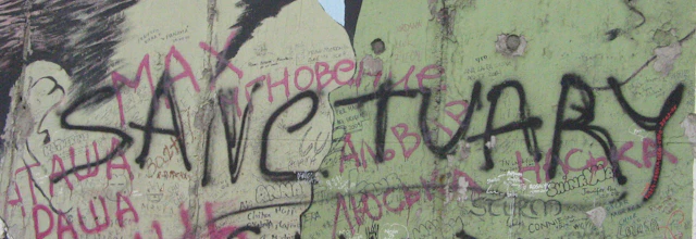 Historisk fragment af Berlinmuren med "Sanctuary" graffiti, der symboliserer frihed og genforening efter Tysklands deling