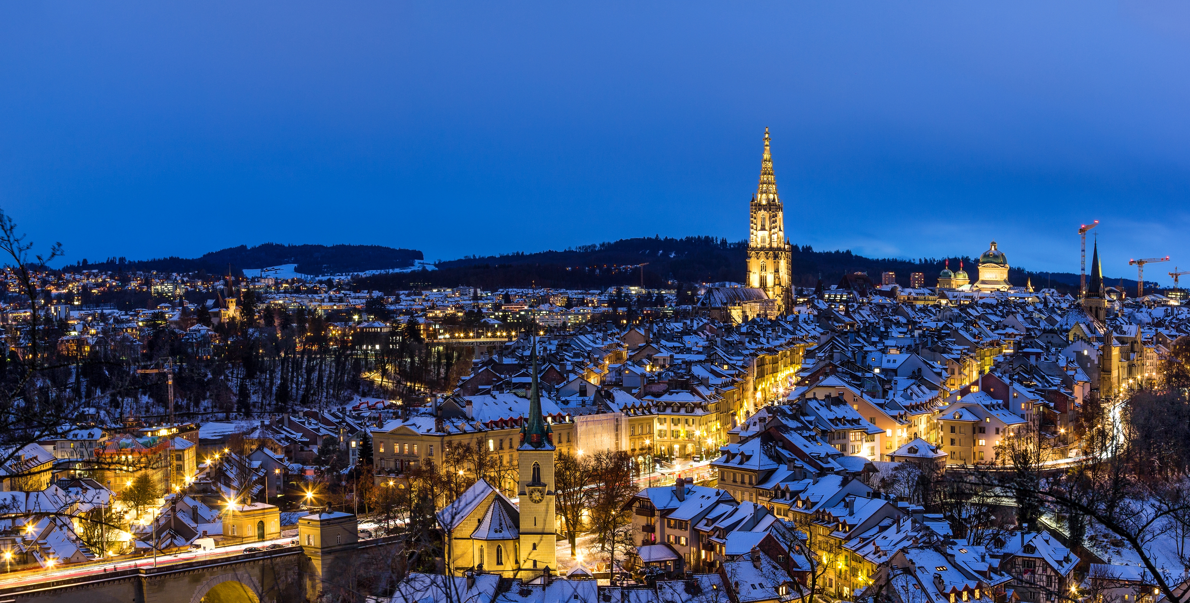 Panoramaudsigt over Berns historiske centrum i vinterens blå time med snedækkede tage og oplyste bygninger set fra Rosengarten, UNESCO-verdensarv i Schweiz