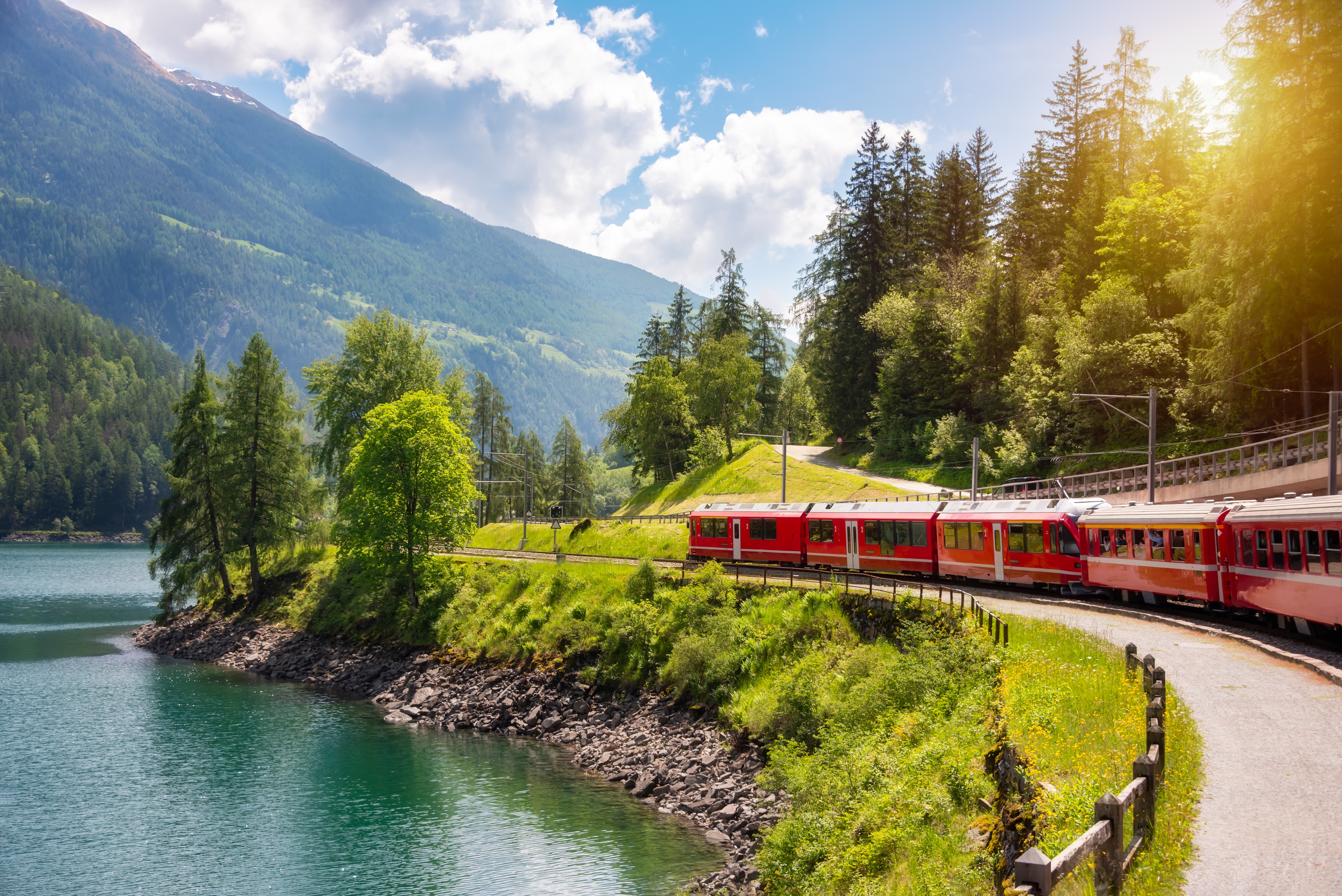 Det ikoniske røde Bernina Express tog kører langs bjerglandskab og sø i de schweiziske alper på en solrig sommerdag