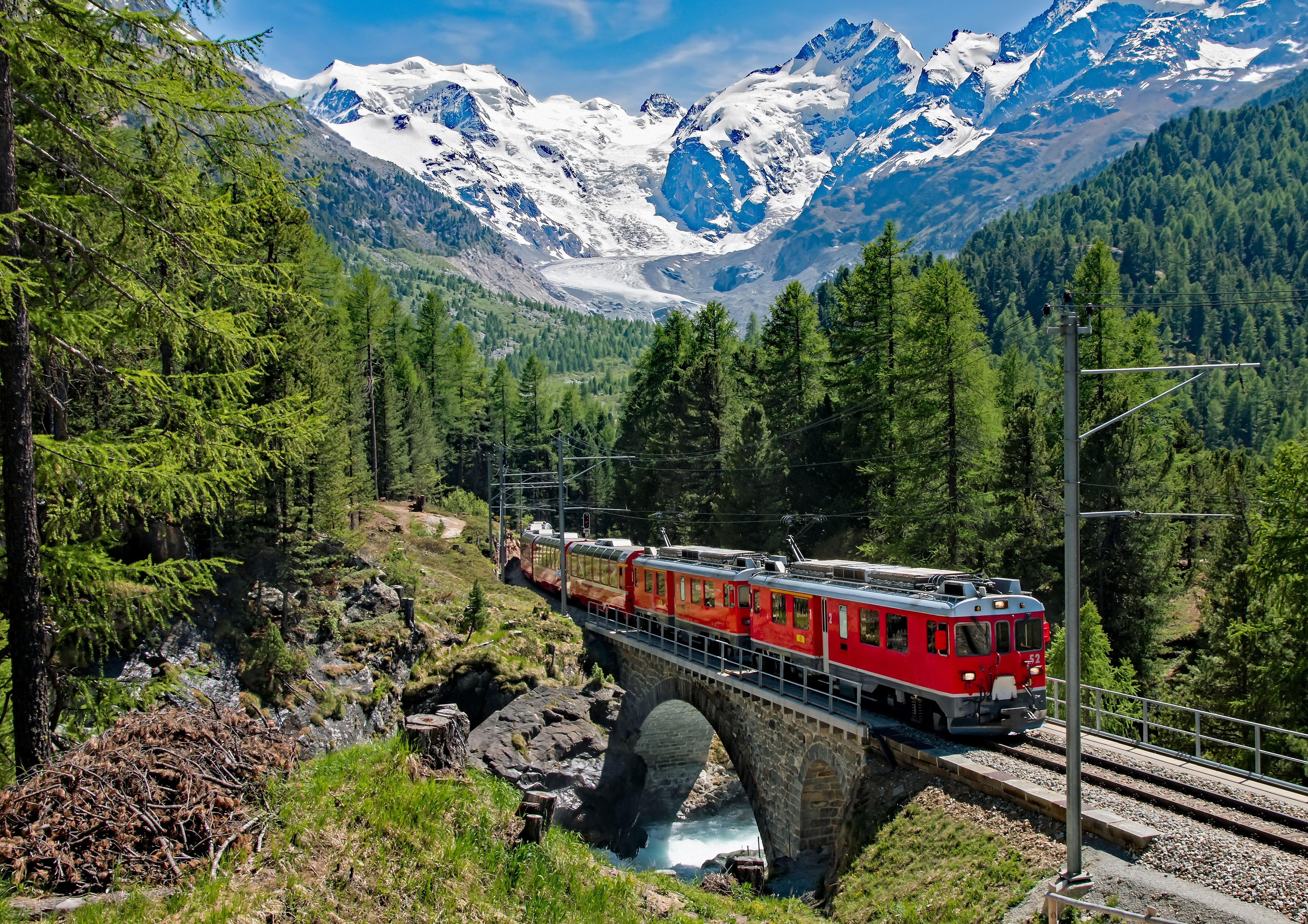 Rødt Bernina Express tog krydser stenbro gennem de schweiziske alper med sneklædte bjerge i baggrunden, UNESCO verdensarv