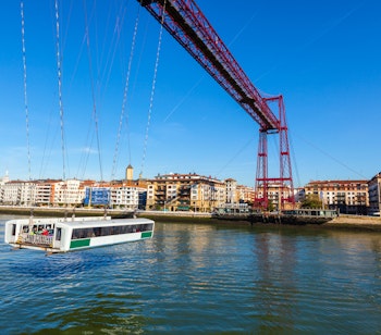 Den historiske Bizkaia-transportbro i Portugalete, Spanien, med den røde stålkonstruktion og gondolfærge, der krydser Nervion-floden