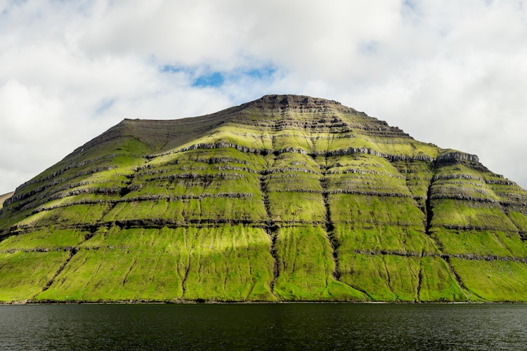 Majestætisk bjerglandskab på Kunoy i Færøerne med solstråler gennem skyerne og atlanterhavets blå vand