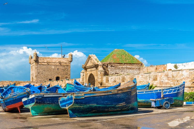 Traditionelle blå fiskerbåde i den historiske havn i Essaouira med byens gamle fæstningsmure i baggrunden, Marokkos charmerende kystby