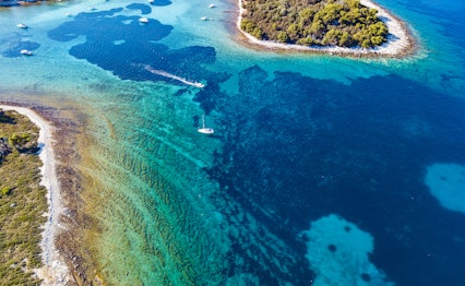 Luftfoto af Den Blå Lagune (Krknjasi) nær Trogir i Kroatien med krystalklart turkisblåt vand, små øer og sejlbåde i Adriaterhavet