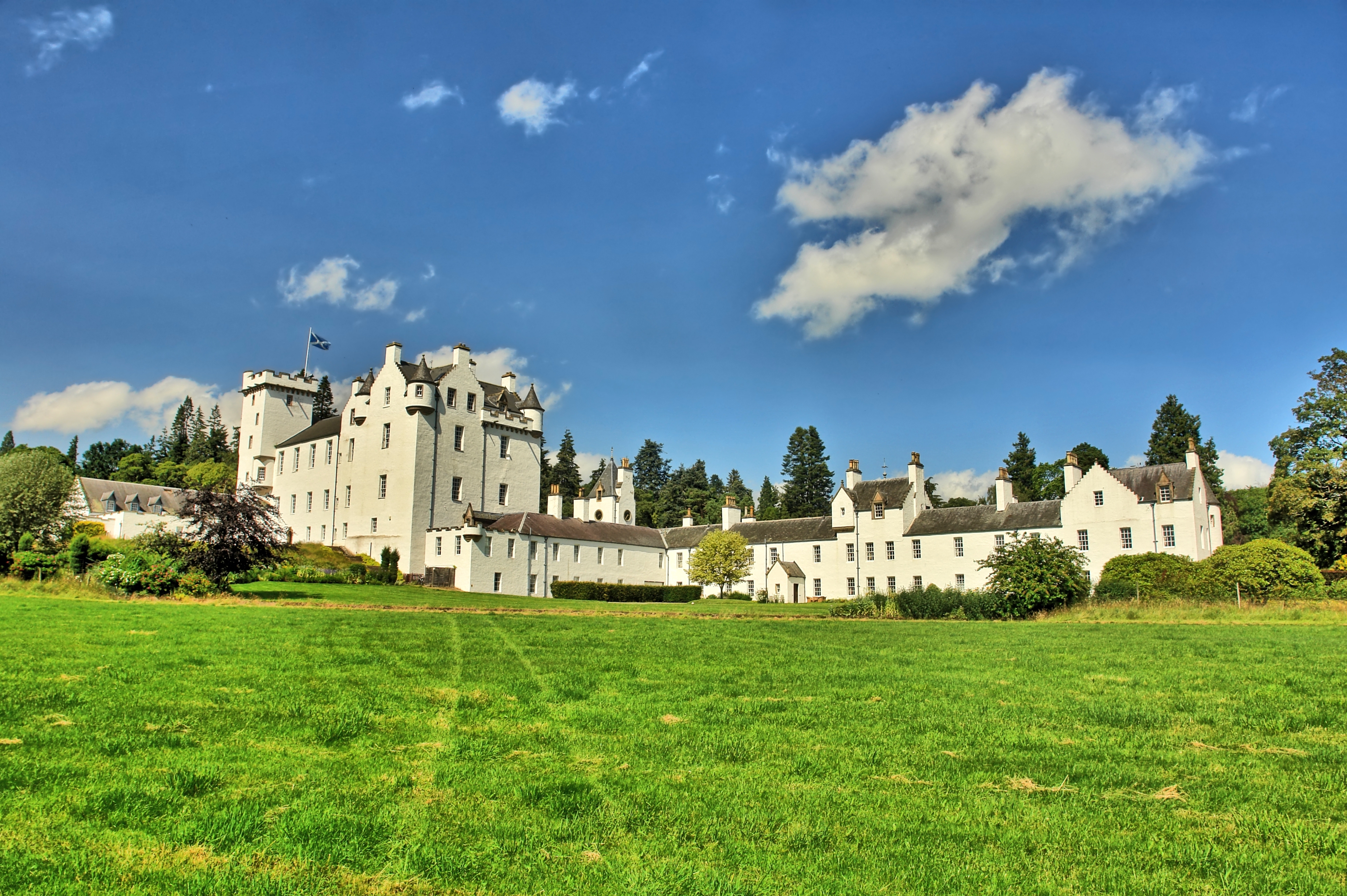 Blair Castle nær landsbyen Blair Atholl i Perthshire, Skotland, med hvide mure, tårne og grønne enge under en klar blå sommerhimmel