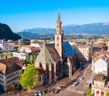 Luftfoto af Bolzanos smukke domkirke med det karakteristiske diamantmønstrede tag og gotisk tårn, omgivet af den historiske bykerne og Alperne i Sydtyrol, Italien