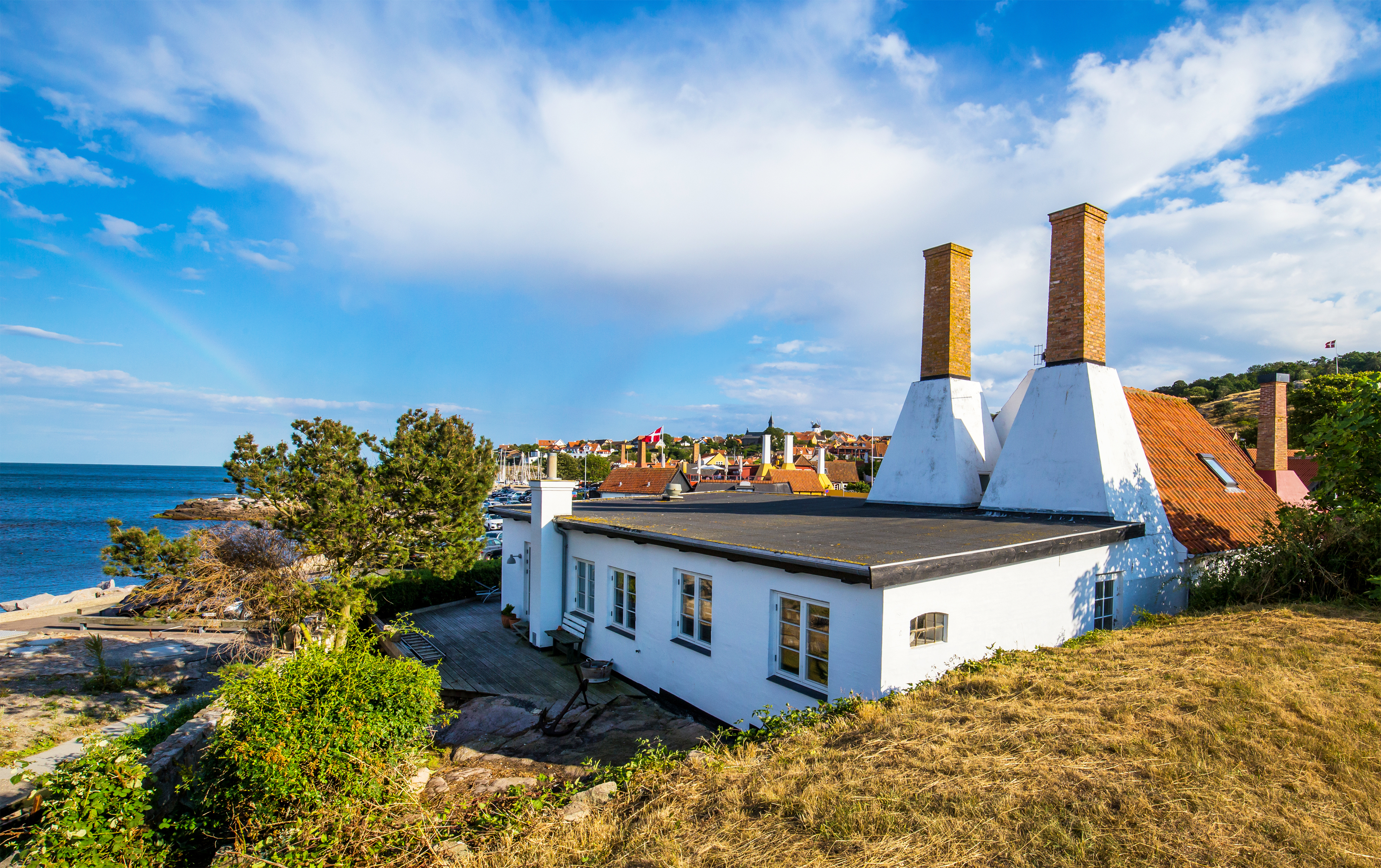 Traditionelt røgeri med karakteristisk skorsten ved den klippefyldte kyst på Bornholm, hvor sild ryges efter gamle håndværkstraditioner i det smukke kystlandskab