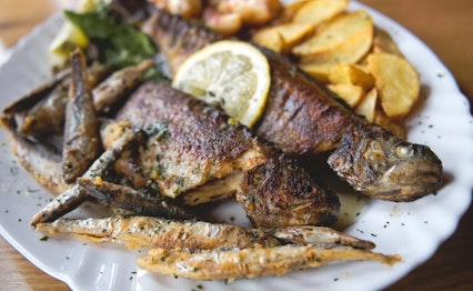 Traditionel bosnisk ret med grillet bjergørred serveret med kartoffel- og løgsalat, hvidløg og citron - en lokal delikatesse fra Bosnien