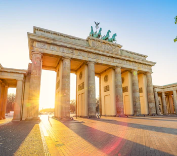 Det ikoniske Brandenburger Tor i Berlin badet i gyldent solnedgangslys, hvor den majestætiske nyklassicistiske arkitektur og den berømte Quadriga-statue fremstår smukt mod aftenhimlen