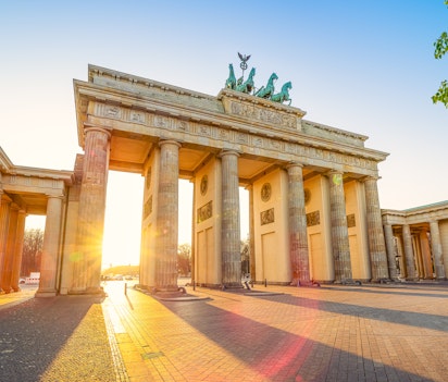 Det ikoniske Brandenburger Tor i Berlin badet i gyldent solnedgangslys, hvor den majestætiske nyklassicistiske arkitektur og den berømte Quadriga-statue fremstår smukt mod aftenhimlen