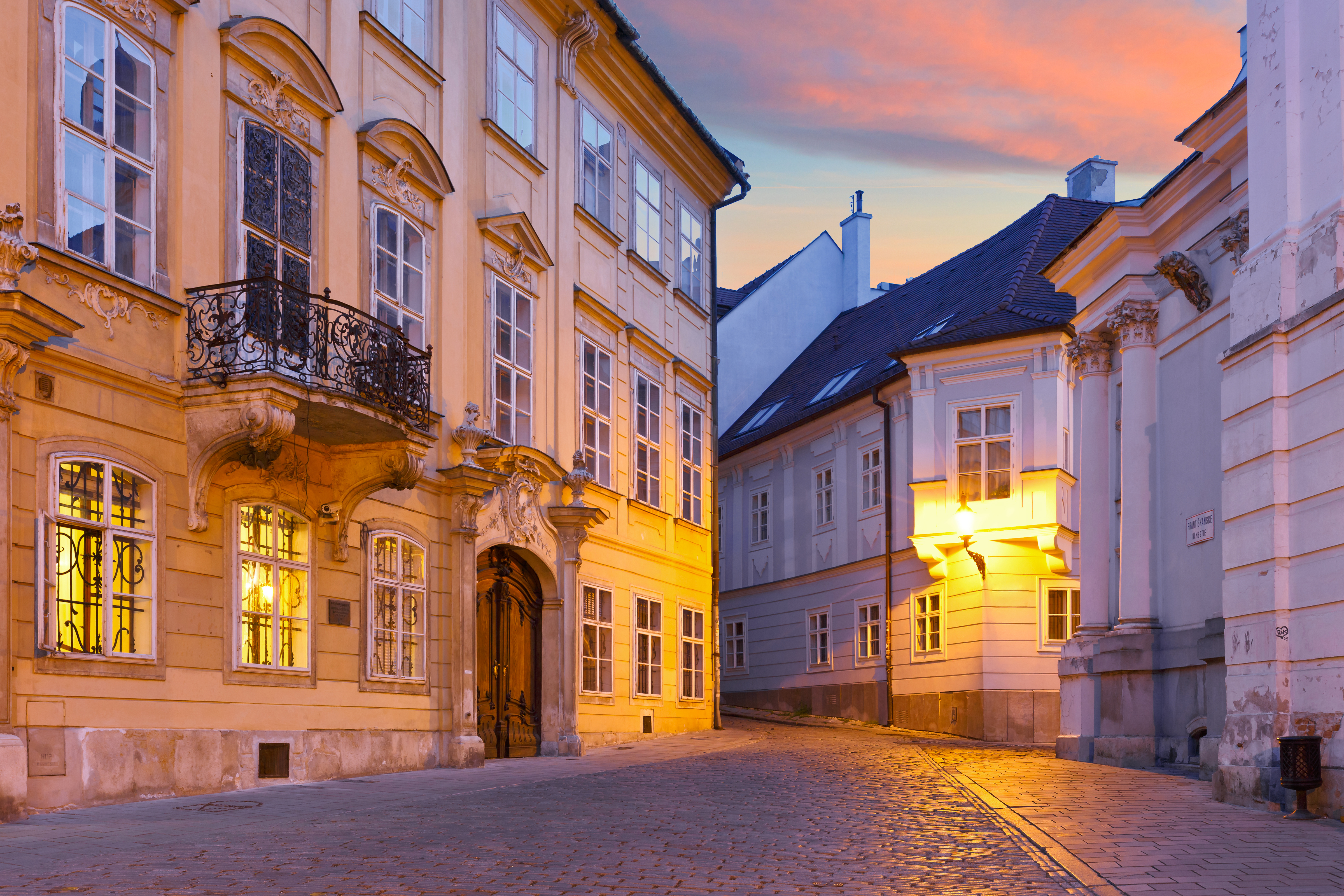 Idyllisk brostensbelagt gade i Bratislavas gamle bydel ved solopgang, med historiske bygninger badet i varmt gyldent lys