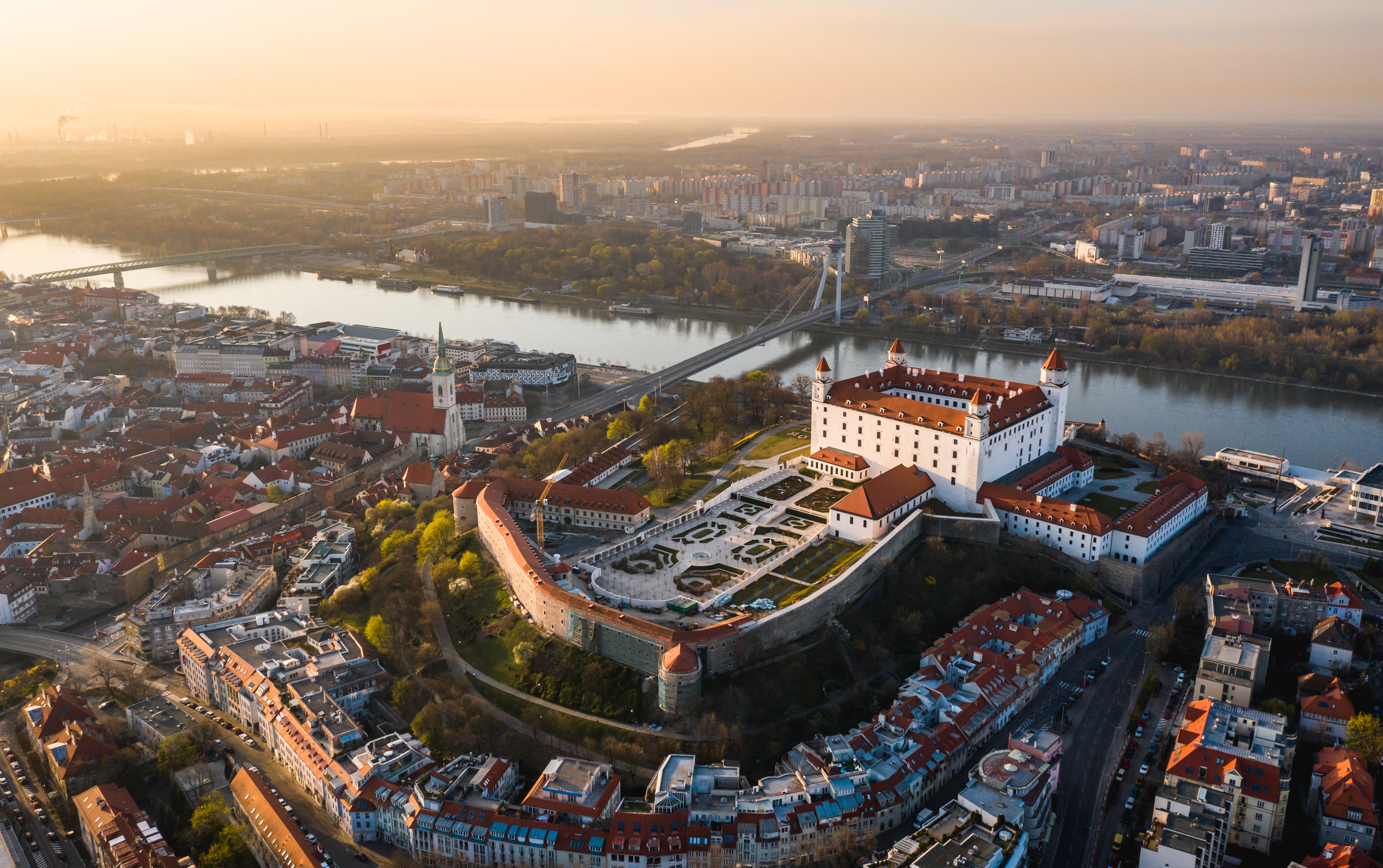 Luftfoto af Bratislava Slot ved Donau-floden i solnedgangslys med historisk gammel by og moderne skyline